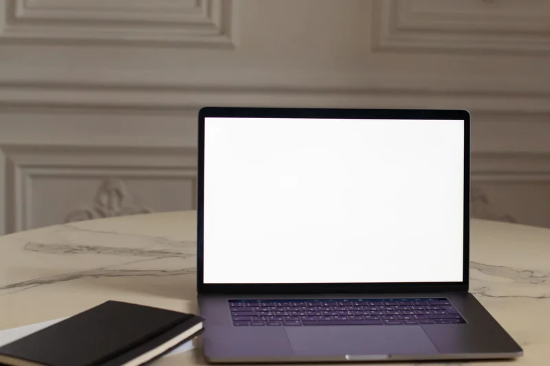 An open laptop and a notebook on a marble table in a room with ivory panelled walls