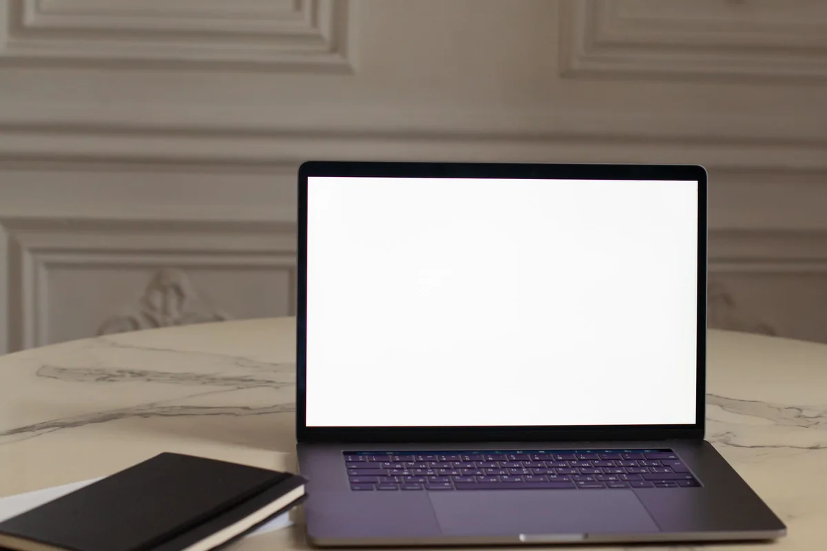An open laptop and a notebook on a marble table in a room with ivory panelled walls